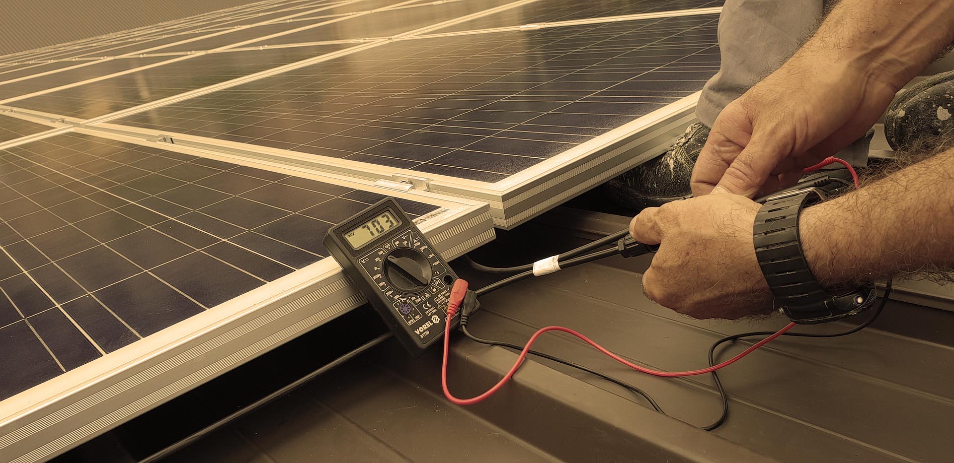 Monter Energii Świetlnej sprawdza miernikiem napięcie na panelach fotowoltaicznych
